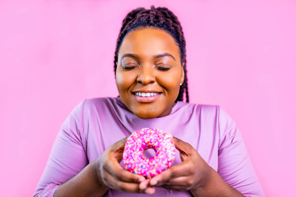 мультикультурна жінка тримає смачний солодкий пончик на рожевому студійному фоні
 - Фото, зображення