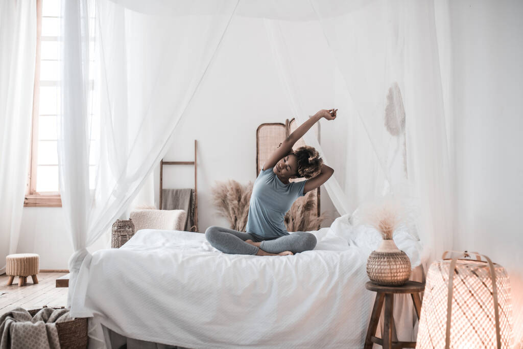 Афроамериканка, сидящая в позе лотоса на кровати - Фото, изображение