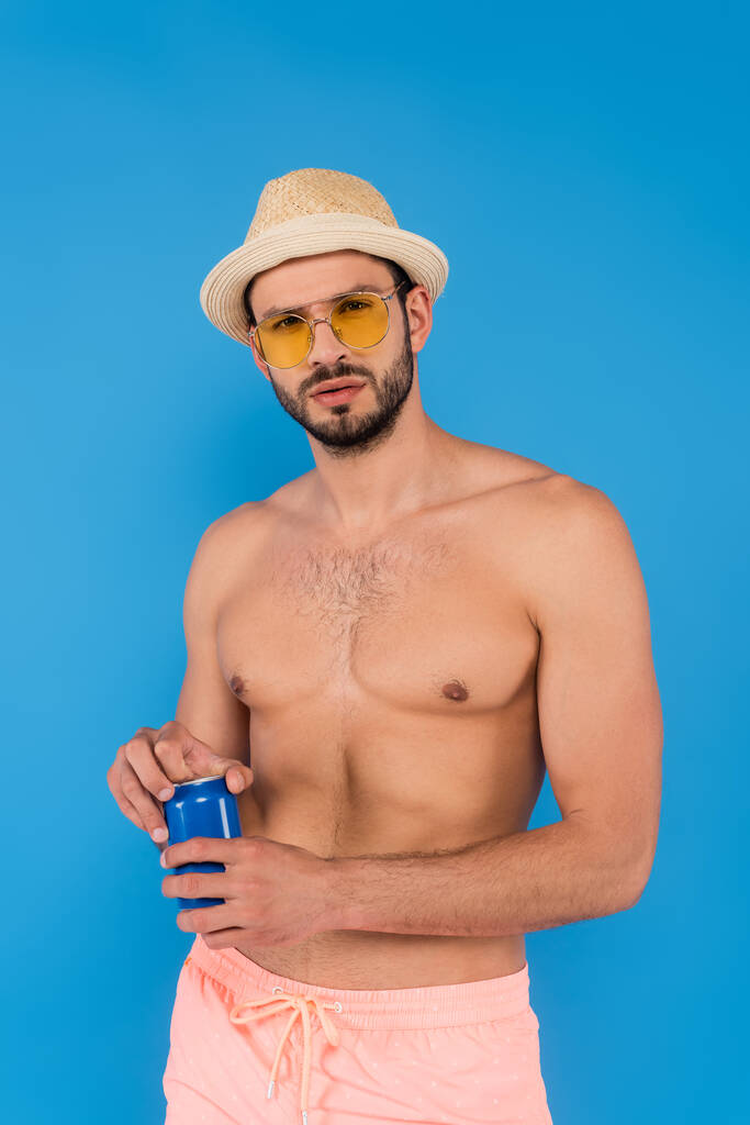 Muž bez košile ve slunečních brýlích drží konzervované nápoje izolované na modré  - Fotografie, Obrázek