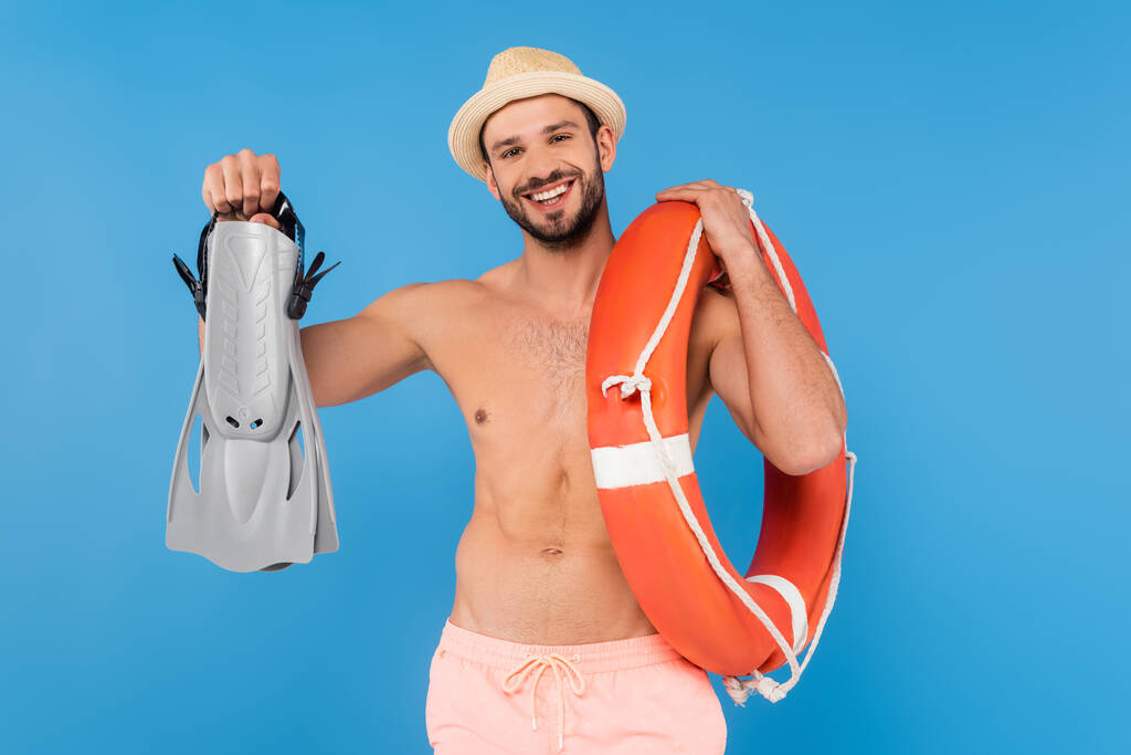 Lächelnder Mann ohne Hemd mit Schwimmflossen und Rettungsboje isoliert auf blauem Grund  - Foto, Bild