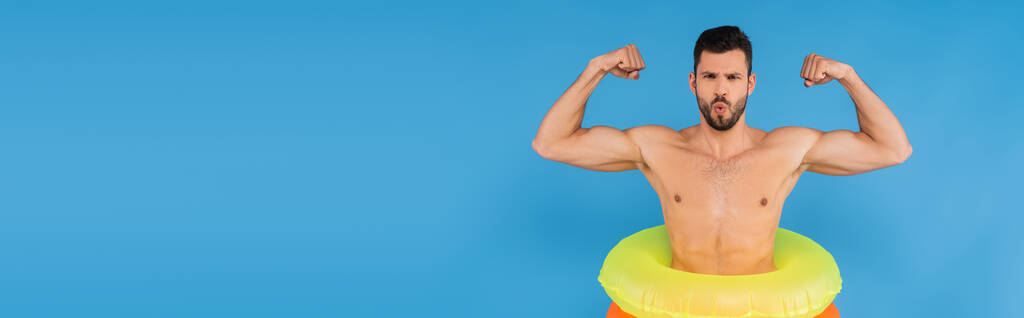 Homem muscular em anéis infláveis mostrando músculos isolados em azul, bandeira  - Foto, Imagem