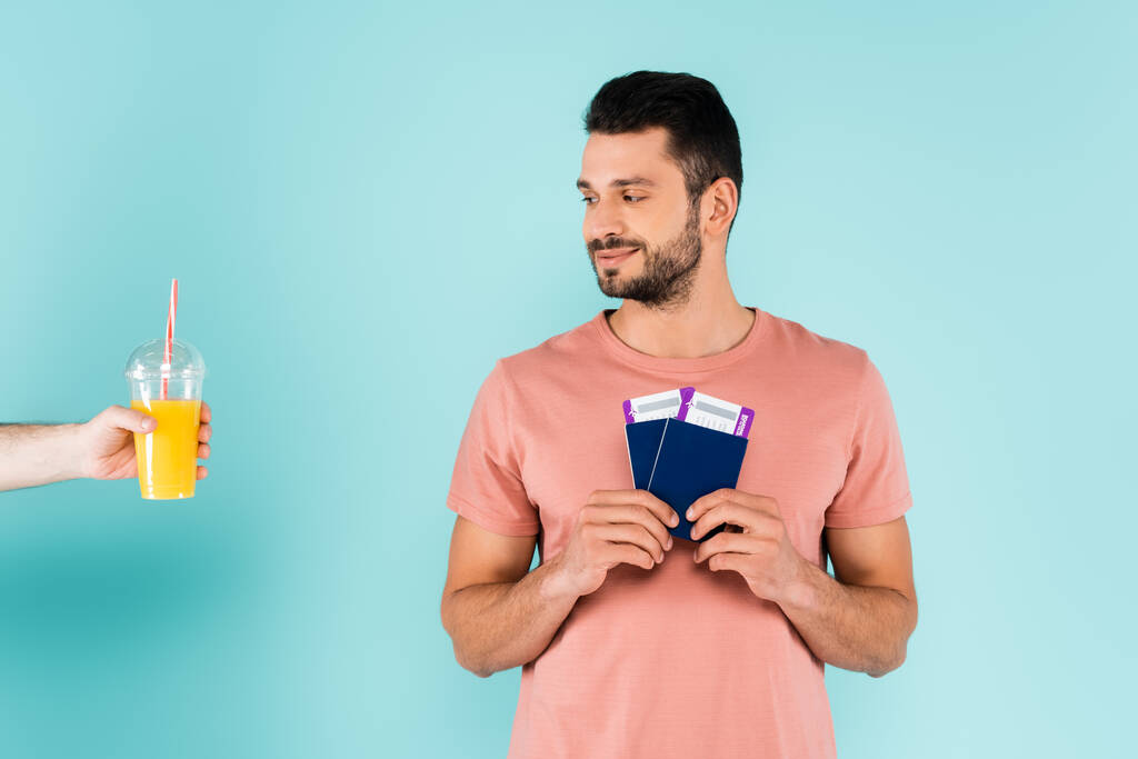 Férfi gazdaság műanyag pohár narancslével közel utazó útlevéllel kék háttér  - Fotó, kép