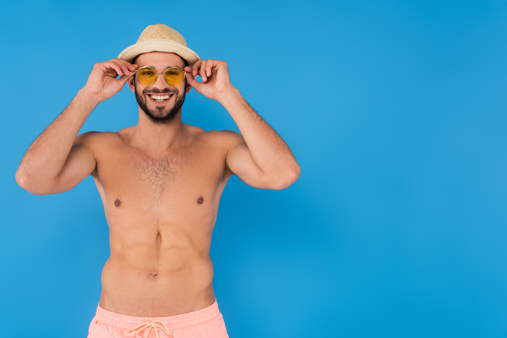 Vidám félmeztelen férfi napszemüvegben és szalmakalap kék háttér  - Fotó, kép