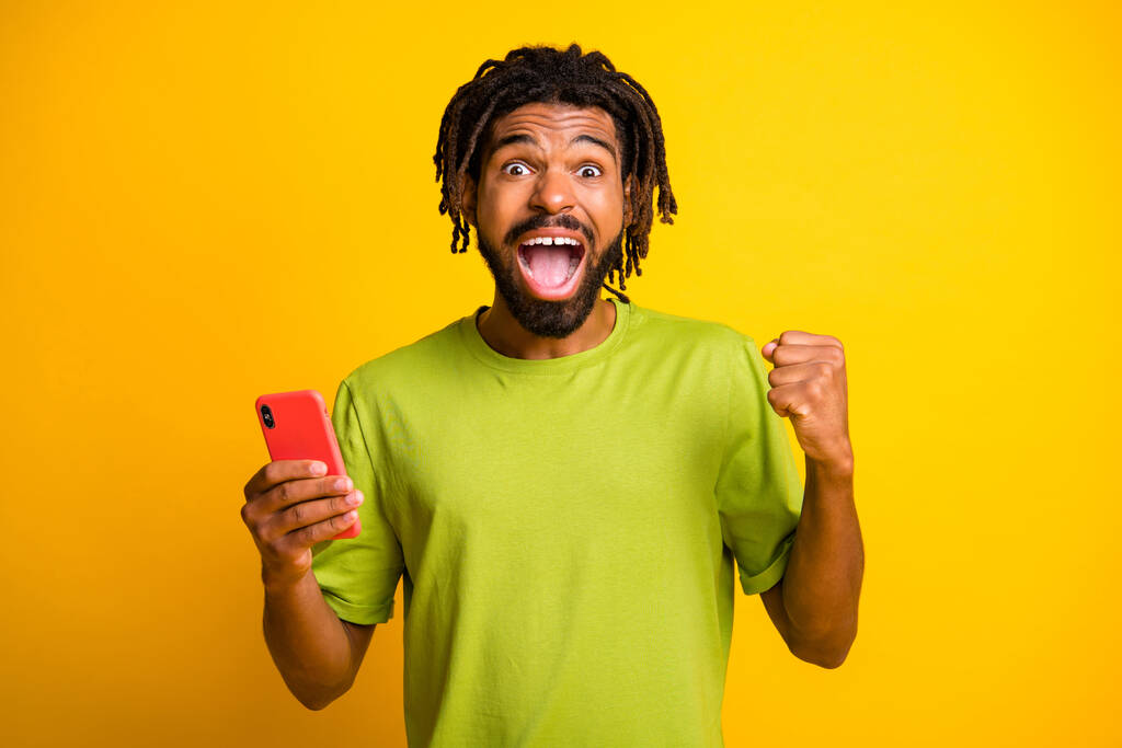 Foto von verrückten dunkelhäutigen Kerl heben Fäuste gewinnen Lotterie Smartphone isoliert über hellem Glanz gelbe Farbe Hintergrund - Foto, Bild