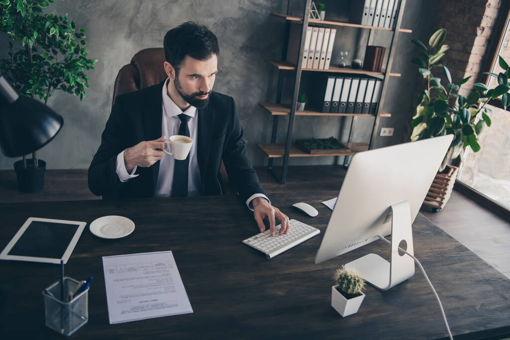 Foto di uomo d'affari fiducioso tenere tazza digitando tastiera sguardo schermo pc indossare cravatta camicia vestito in ufficio moderno all'interno - Foto, immagini