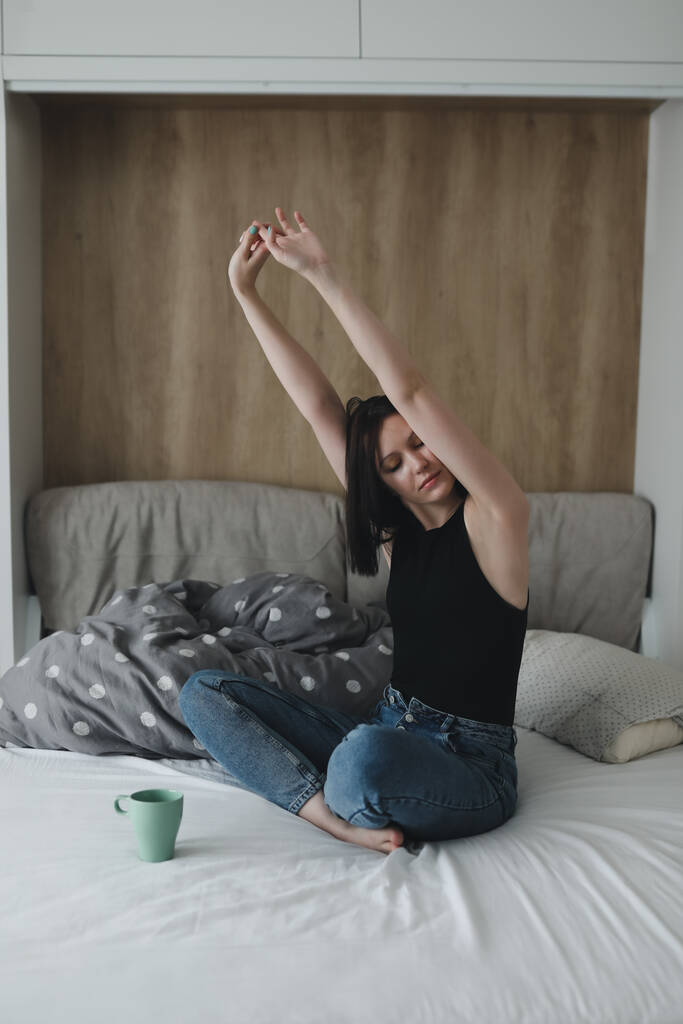 Νεαρή γυναίκα το πρωί στο κρεβάτι με ένα φλιτζάνι καφέ - Φωτογραφία, εικόνα