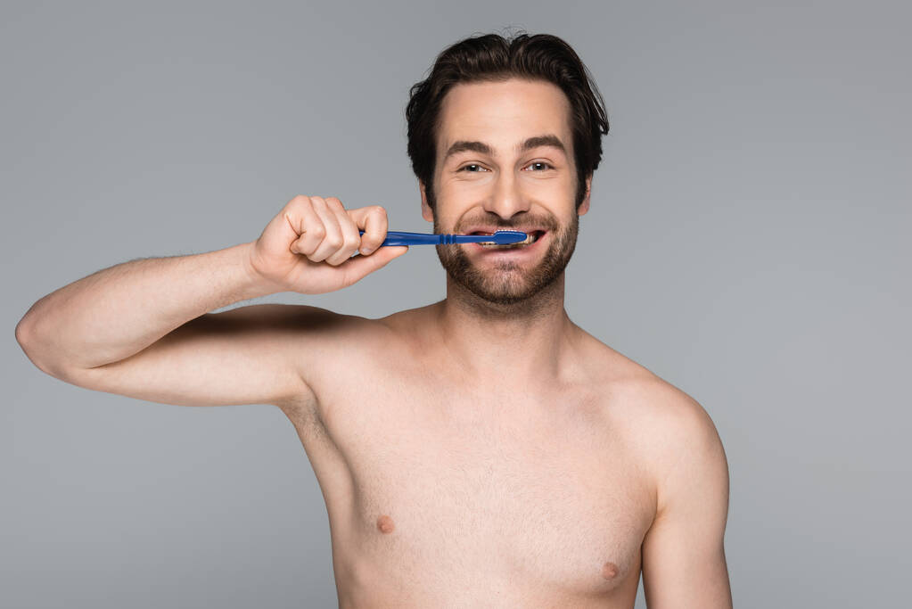 usmívající se muž bez košile čistí zuby izolované na šedi - Fotografie, Obrázek
