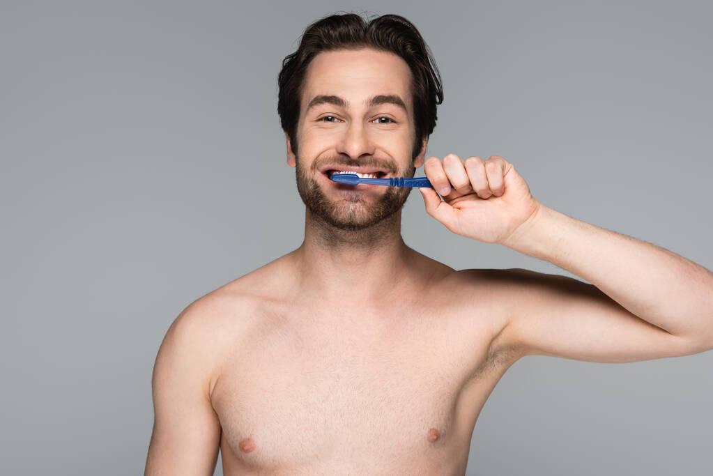 gelukkig en shirtloos man poetsen tanden geïsoleerd op grijs - Foto, afbeelding