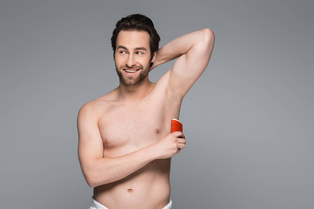 веселий без сорочки чоловік наносить твердий дезодорант палички ізольований на сірому
 - Фото, зображення