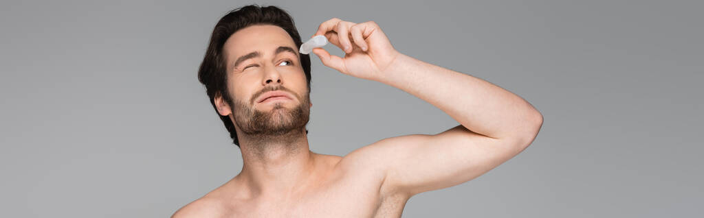 homme torse nu avec oeil fermé appliquant des gouttes ophtalmiques isolées sur gris, bannière - Photo, image