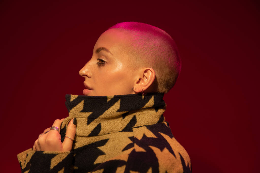 Female with nude makeup wearing stylish jacket posing at studio with red wall - Foto, afbeelding
