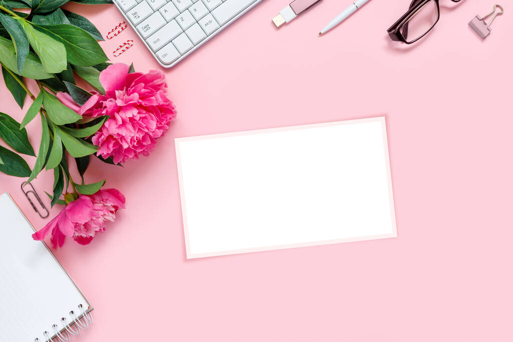 Laptop, accessoires en boeket van prachtige pioenen met bril en koptelefoon op roze achtergrond. Platte werkplaats.  - Foto, afbeelding