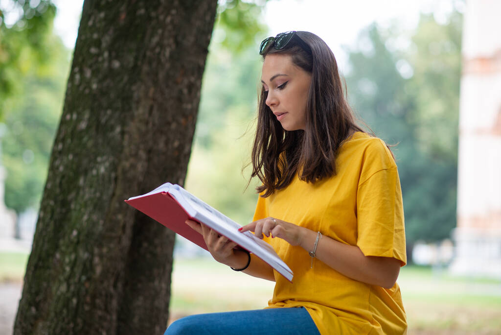 Young woman student writing on a book outdoor in a park - Photo, Image