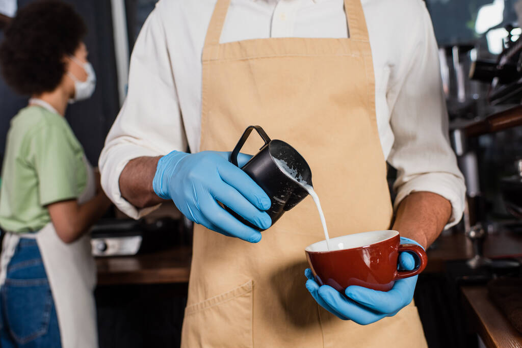 Barista afroamericano in guanti di lattice che fa il caffè con il latte nel caffè  - Foto, immagini
