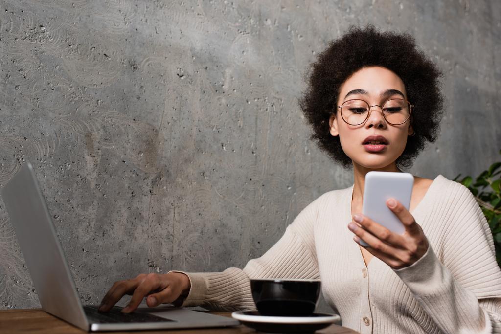 Африканська американка використовує ноутбук і смартфон біля чашки в кафе.  - Фото, зображення
