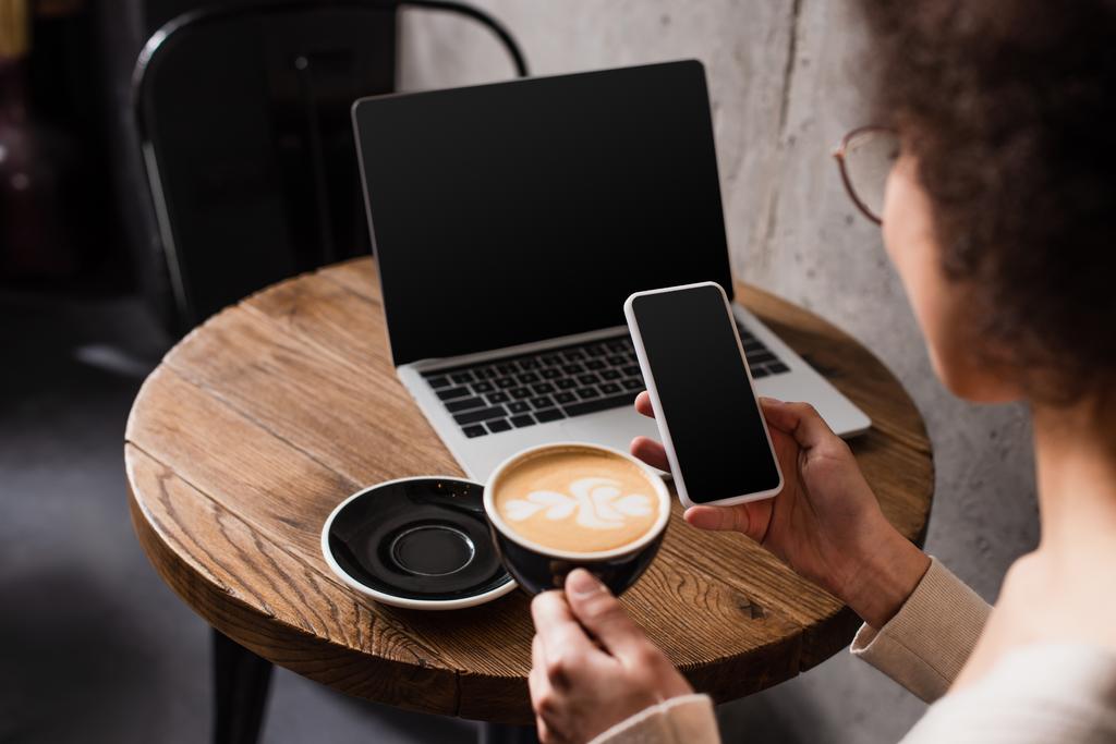Smartphone και καφέ στα χέρια του θολή αφροαμερικανού ελεύθερου επαγγελματία στο καφέ  - Φωτογραφία, εικόνα