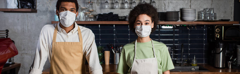 Baristas afroamericanos en máscaras médicas mirando a la cámara en el café, pancarta  - Foto, Imagen