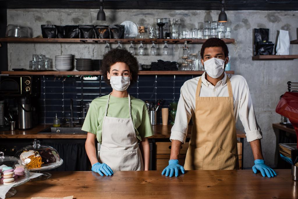 Африканские американские баристы в латексных перчатках и медицинских масках стоят в кафе  - Фото, изображение