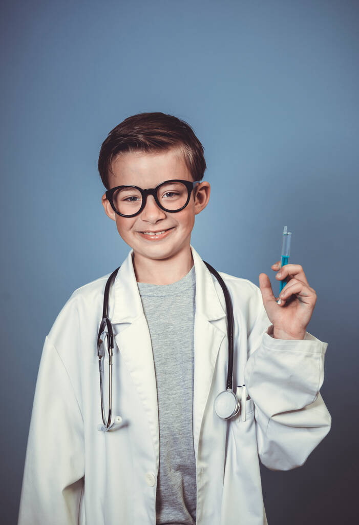 крутий молодий хлопчик маскується як лікар з білим димом і грає зі шприцом і стетоскопом перед синім тлом
 - Фото, зображення