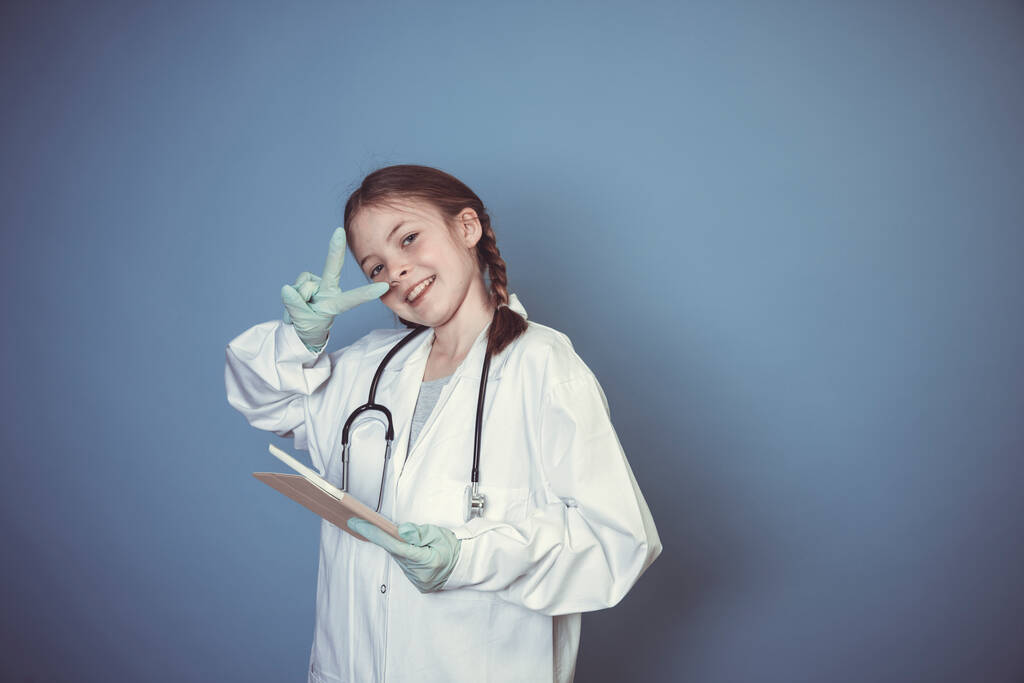 bella ragazza vestita da medico con guanti verdi e tablet digitale davanti a sfondo blu - Foto, immagini