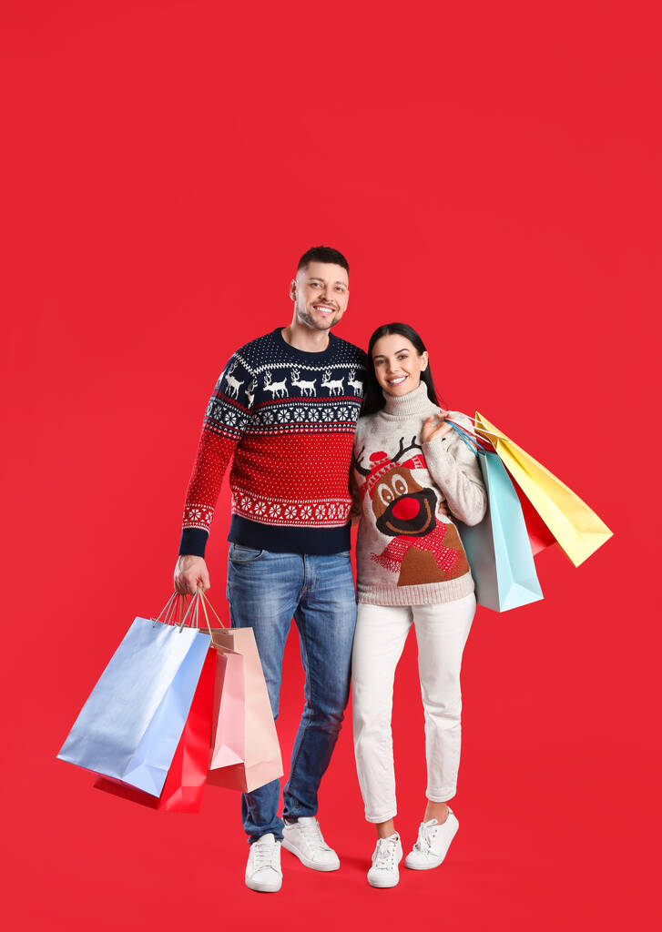 赤い背景に紙袋を持つ幸せなカップル。クリスマスショッピング - 写真・画像
