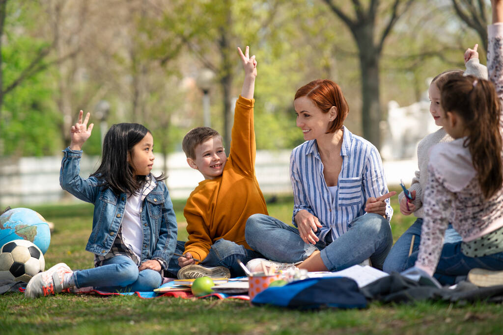 Учитель с маленькими детьми, сидящий на открытом воздухе в городском парке, концепция группового образования. - Фото, изображение