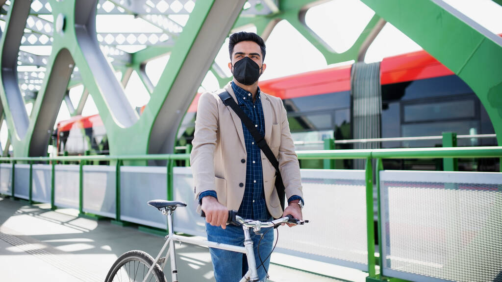 Молодой бизнесмен пригородный с велосипедом собирается работать на открытом воздухе на мосту в городе, коронавирусная концепция. - Фото, изображение