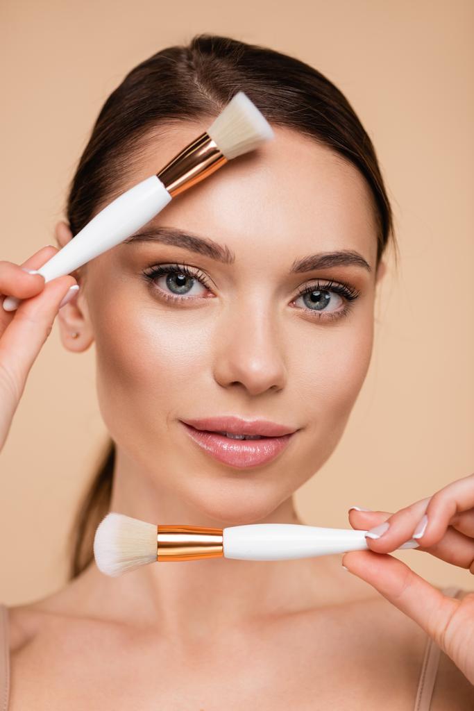 portrait of pretty woman with perfect skin holding cosmetic brushes isolated on beige - Photo, Image