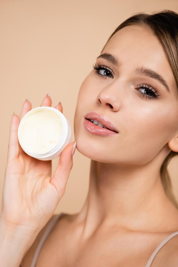 portrait of pretty woman with perfect skin holding cosmetic cream isolated on beige - Photo, Image