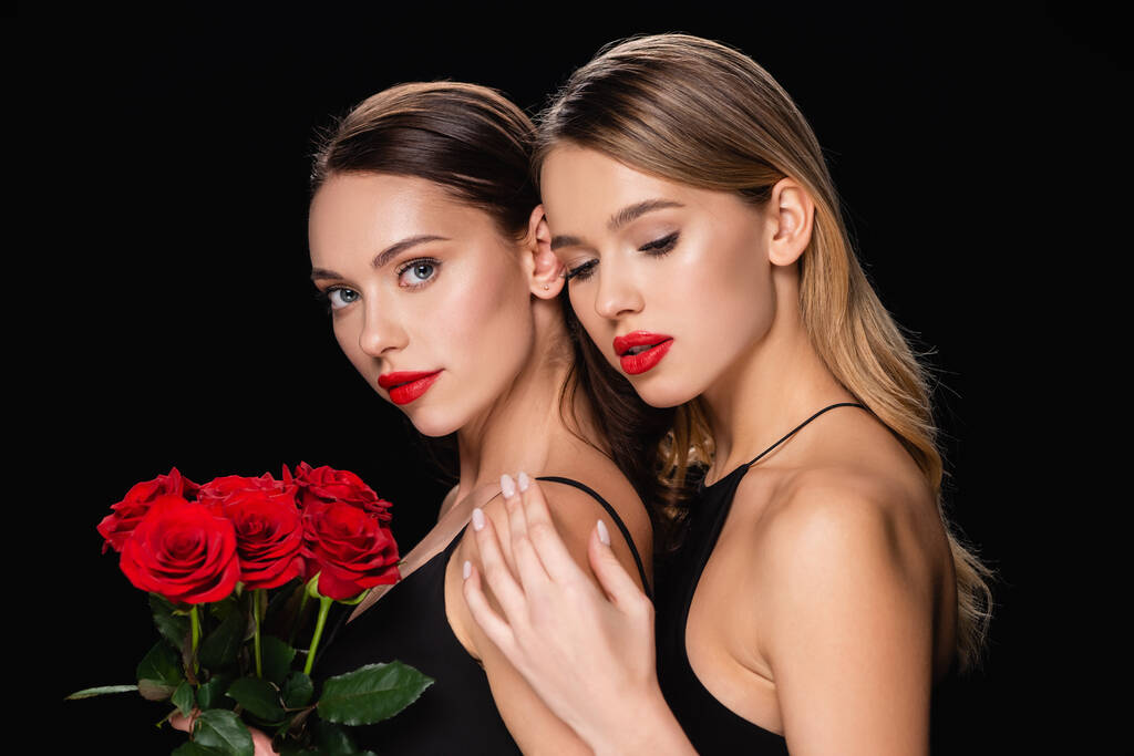 красива жінка торкається плеча чарівного друга, який тримає червоні троянди ізольовані на чорному
 - Фото, зображення