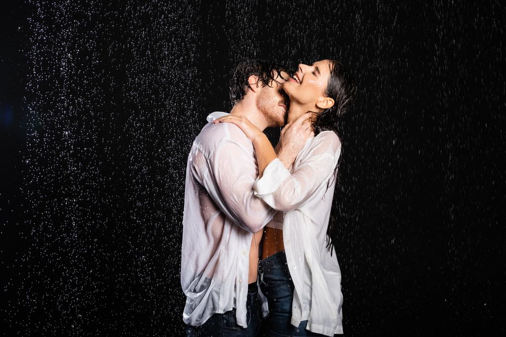 romantický přítel objímání se sexy přítelkyně v mokrém oblečení v dešti kapky na černém pozadí - Fotografie, Obrázek