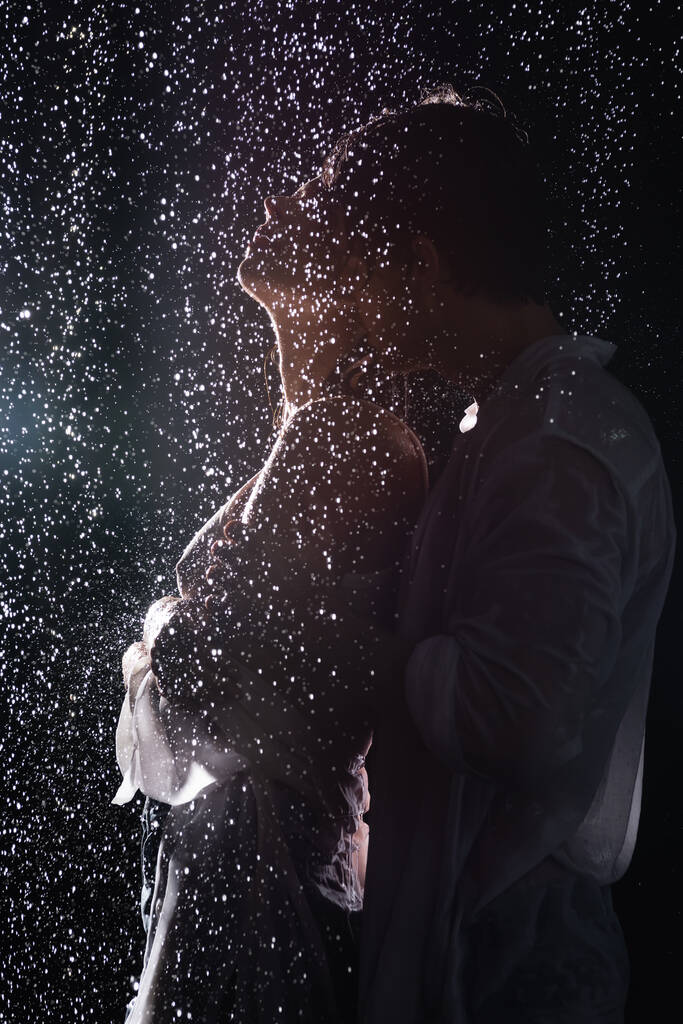 σέξι ρομαντικό ζευγάρι αγκαλιάζει παθιασμένα σε σταγόνες βροχής σε μαύρο φόντο με πίσω φως - Φωτογραφία, εικόνα