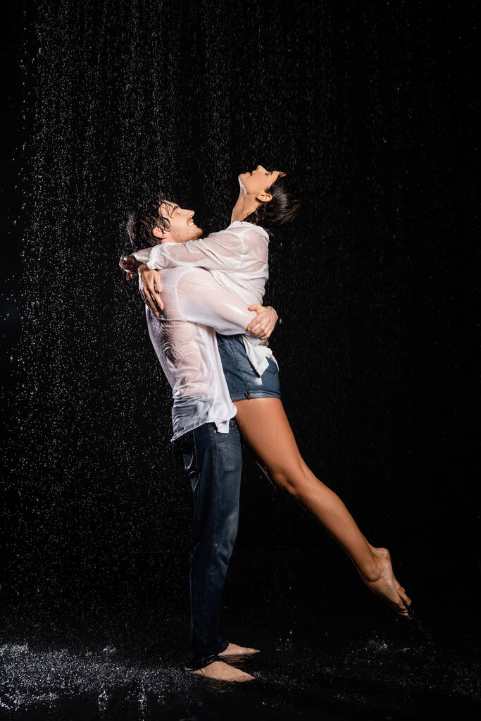 雨の中で抱きつく幸せと情熱的なロマンチックなカップルが黒の背景に落ちる - 写真・画像