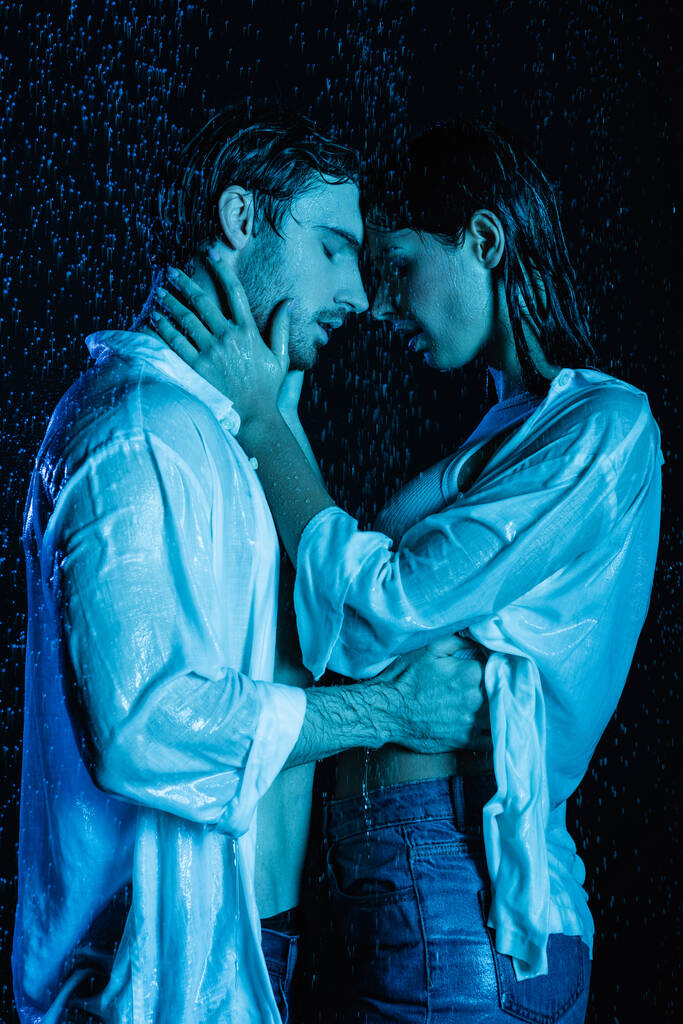 couple romantique passionné embrasser doucement dans des gouttes d'eau sur fond noir avec filtre de couleur bleue  - Photo, image