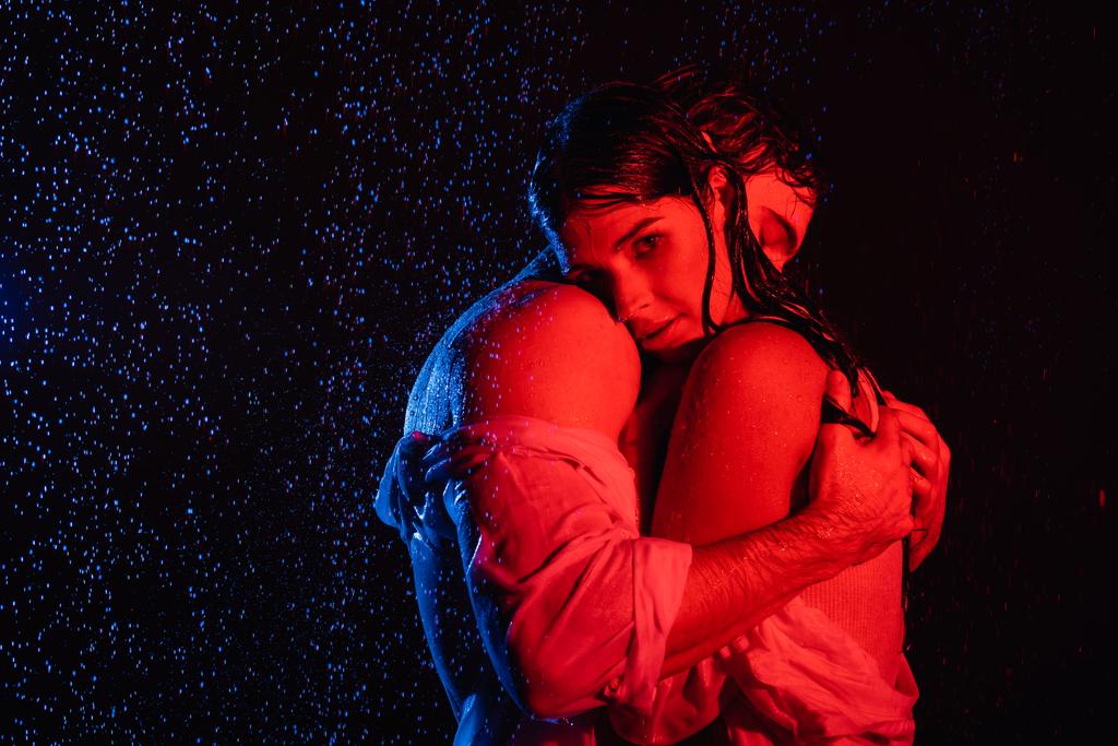 filtros de colores rojo y azul imagen de pareja romántica apasionada húmeda abrazándose suavemente en gotas de agua sobre fondo negro - Foto, imagen