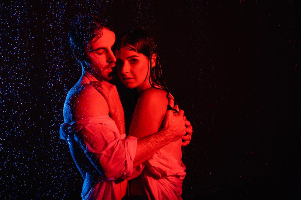 czerwone i niebieskie kolory filtry obraz mokrej namiętnej romantycznej pary przytulającej się w kroplach wody na czarnym tle - Zdjęcie, obraz