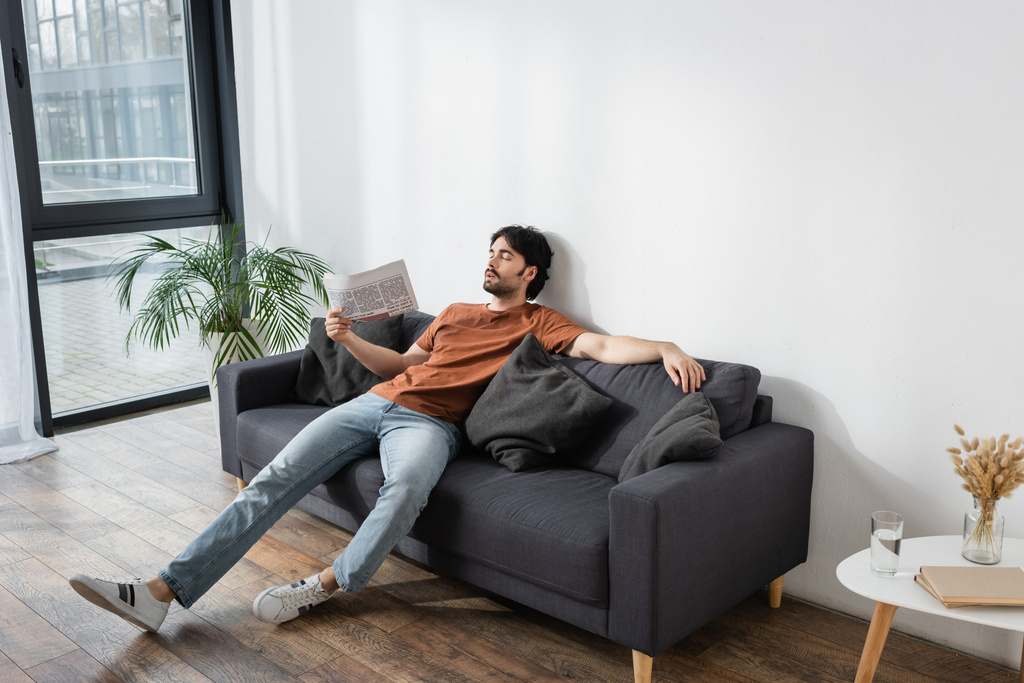 homme agitant avec journal tout en étant couché sur un canapé gris et souffrant de chaleur - Photo, image