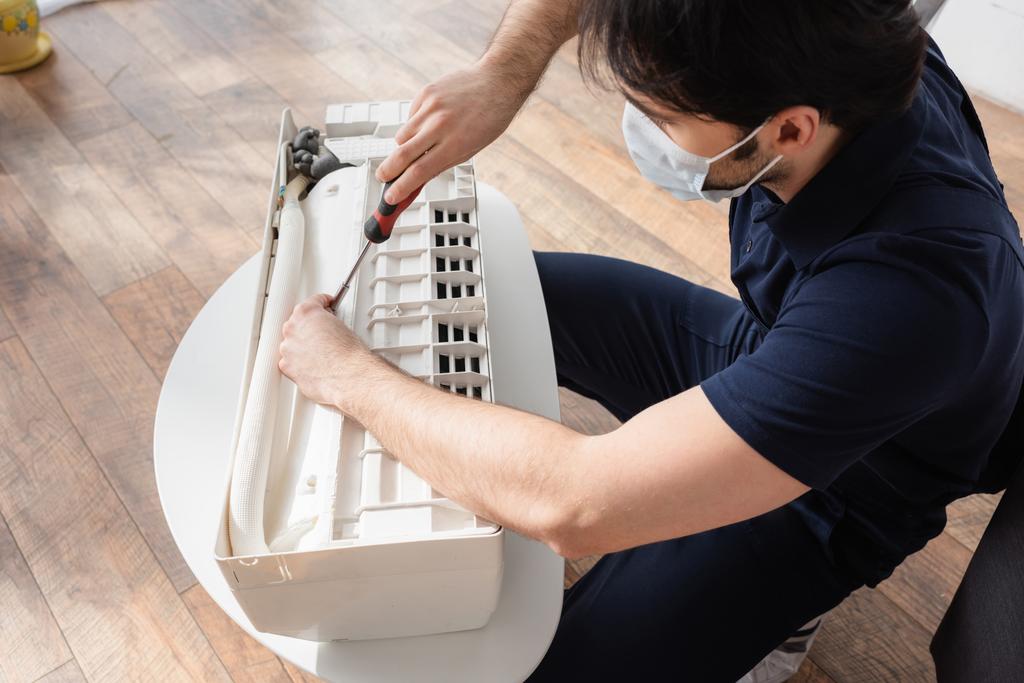 Handwerker in medizinischer Maske repariert defekte Klimaanlage  - Foto, Bild