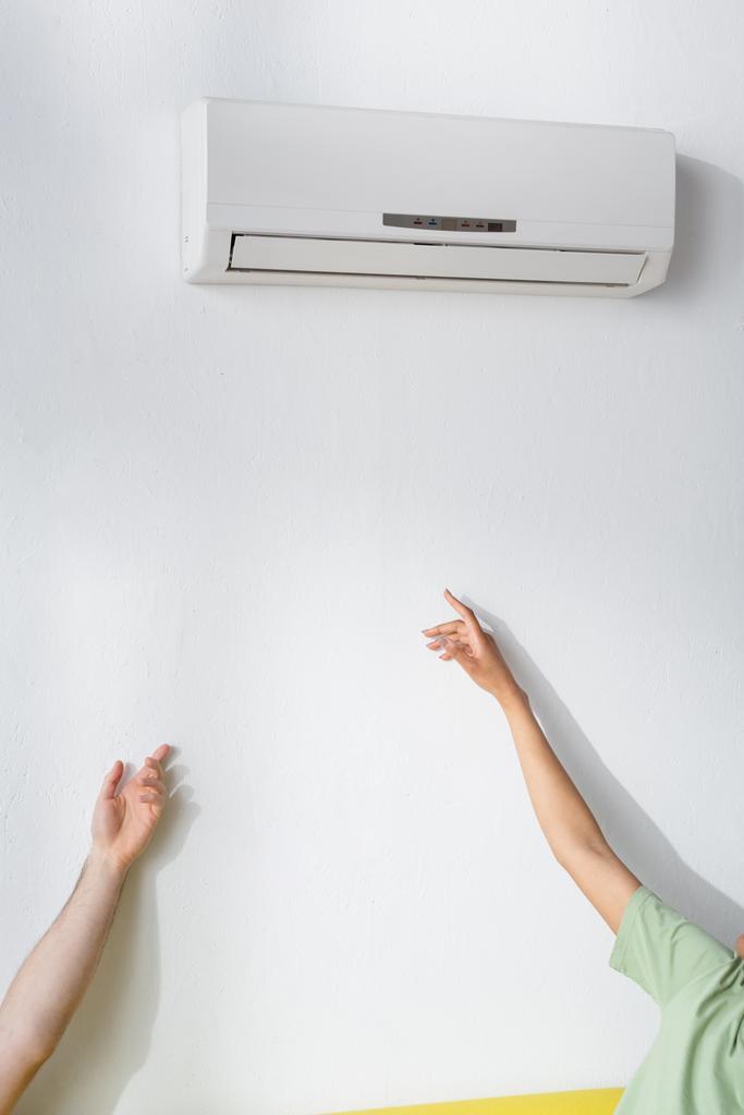abgeschnittene Ansicht von multiethnischen Paar, das Klimaanlage erreicht, während es im Sommer unter Hitze leidet - Foto, Bild
