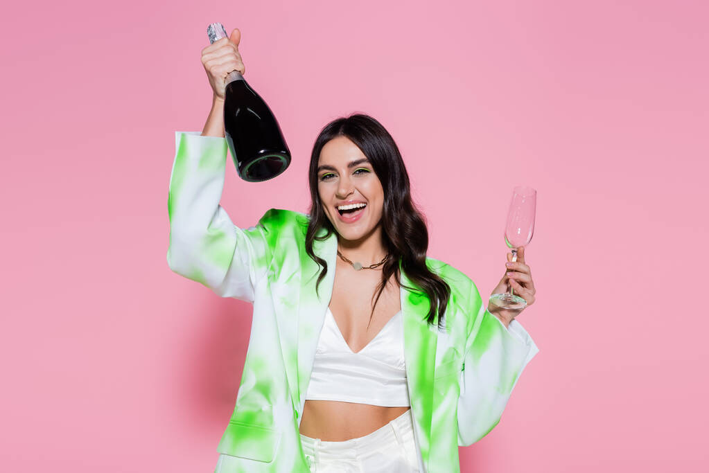 Положительная женщина держит бутылку шампанского на розовом фоне  - Фото, изображение