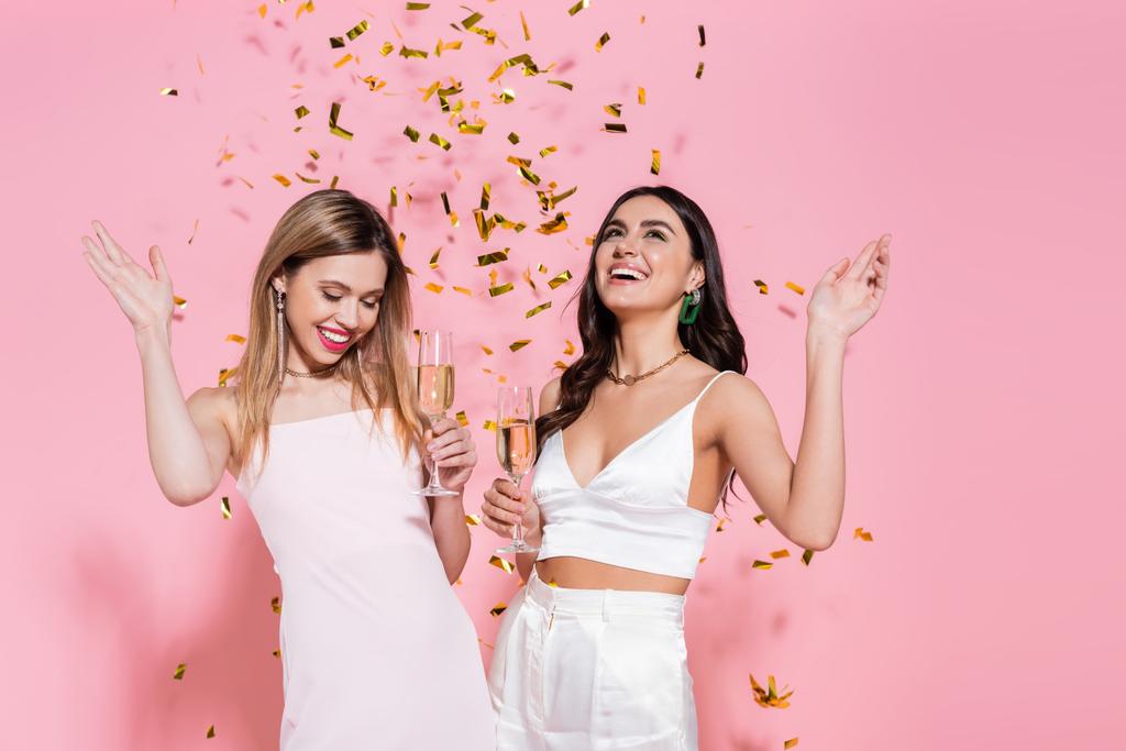 Красивые друзья держат шампанское под падать конфетти на розовом фоне  - Фото, изображение