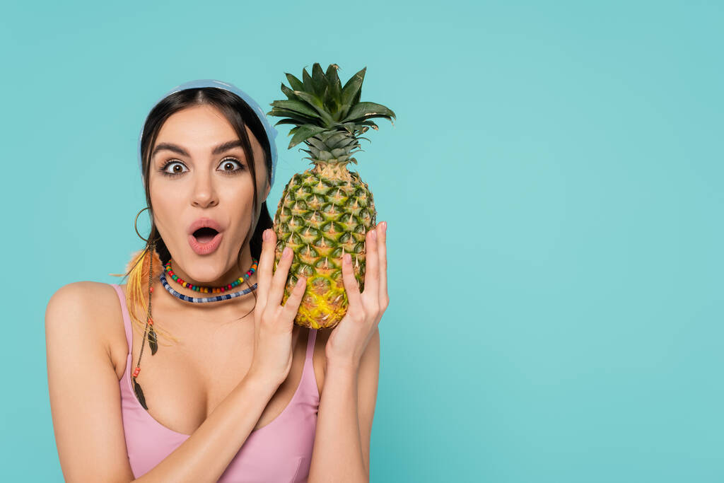 Excited woman in bandana holding pineapple isolated on blue  - Photo, Image