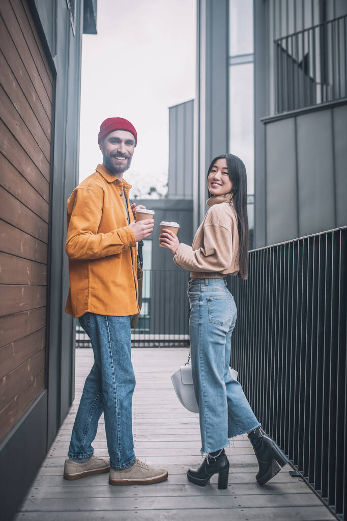Junger Mann und Frau in lässiger Kleidung sehen beim Kaffee im Freien positiv aus - Foto, Bild