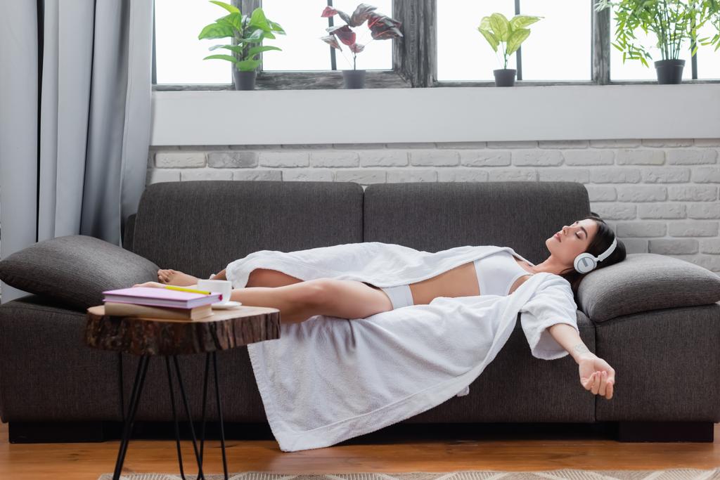 junge erwachsene Frau schläft in Kopfhörern auf Couch zu Hause - Foto, Bild