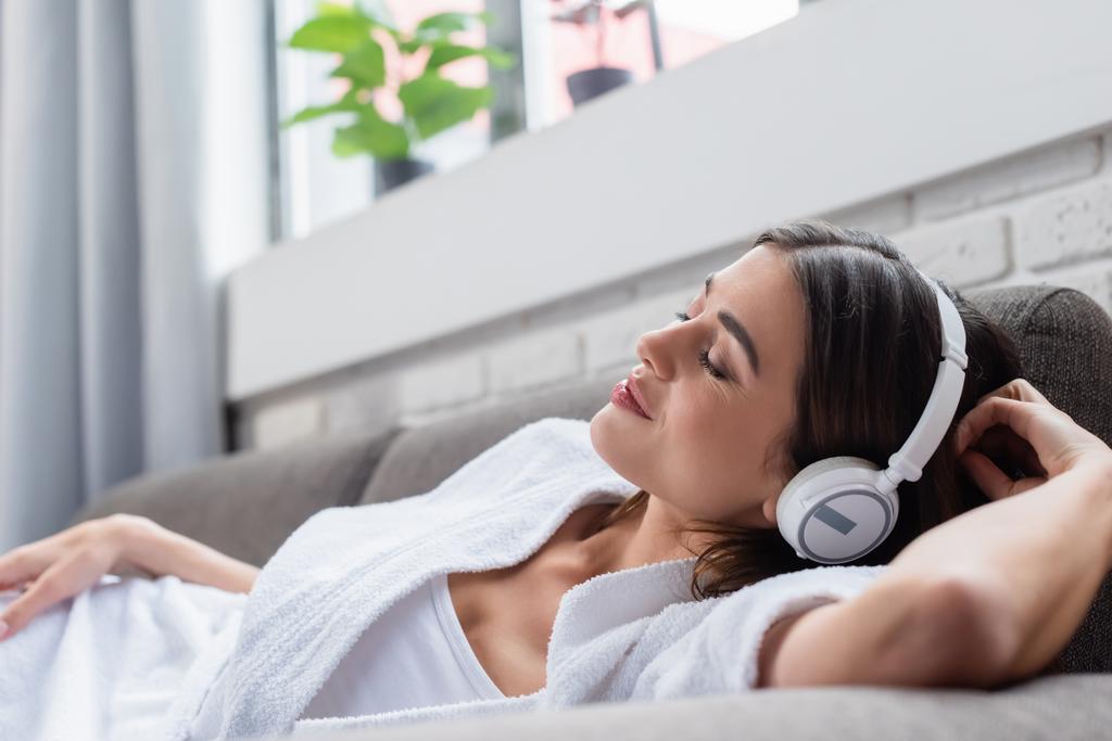 peaceful young adult woman with closed eyes resting in headphones on couch at home - Photo, Image