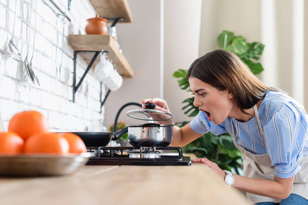 malestar joven mujer adulta cocina cerca de quemador en la cocina moderna - Foto, imagen