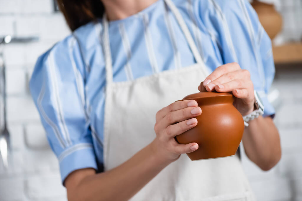 vista parziale della giovane donna adulta che tiene la pentola di argilla in mano in cucina - Foto, immagini