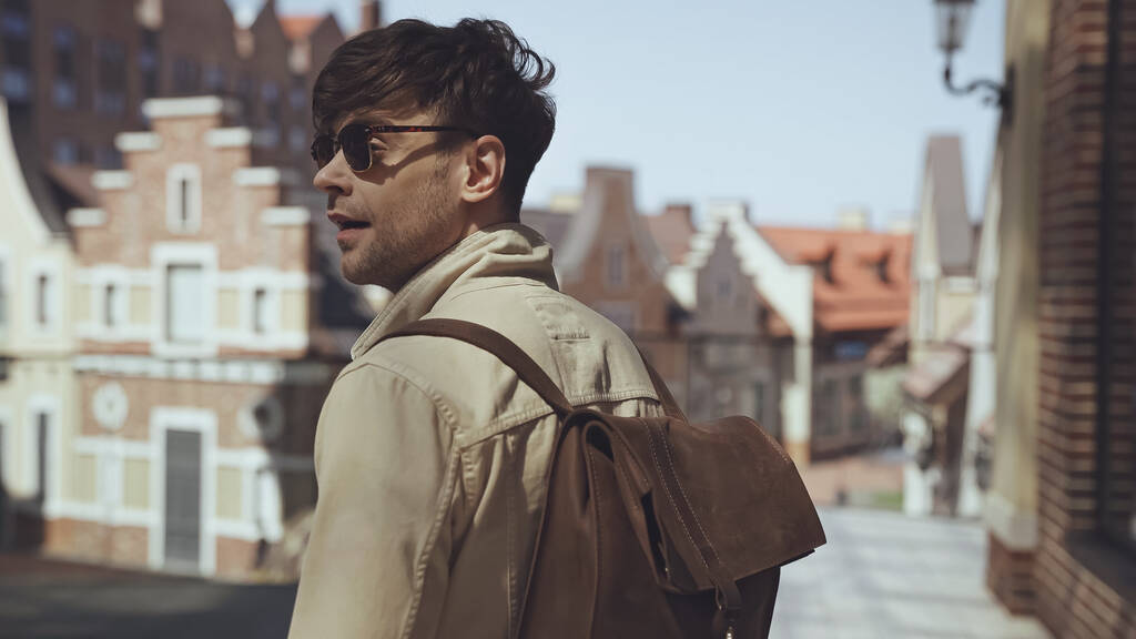 Güneş gözlüklü ve sırt çantalı şık bir turist dışarıda bekliyor. - Fotoğraf, Görsel