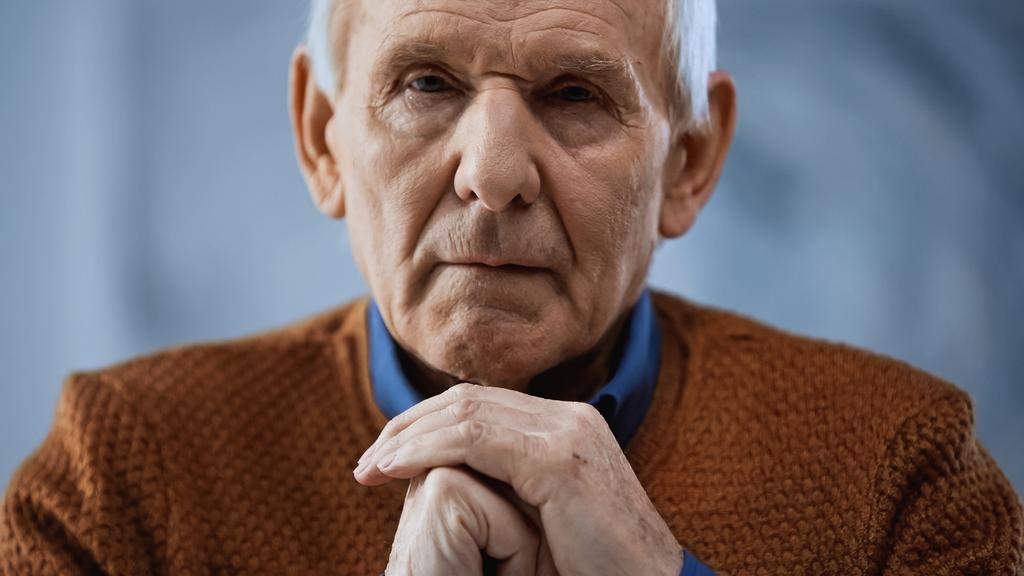 Porträt eines älteren Mannes mit geballten Händen in Gesichtsnähe auf grauem Hintergrund - Foto, Bild