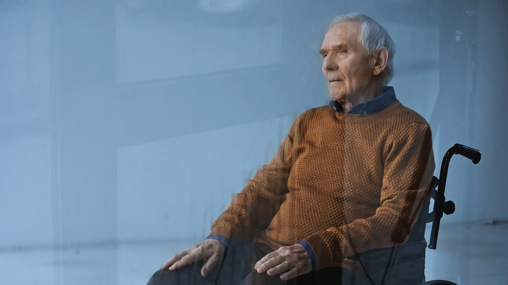 uomo anziano premuroso in sedia a rotelle guardando lontano su sfondo grigio - Foto, immagini